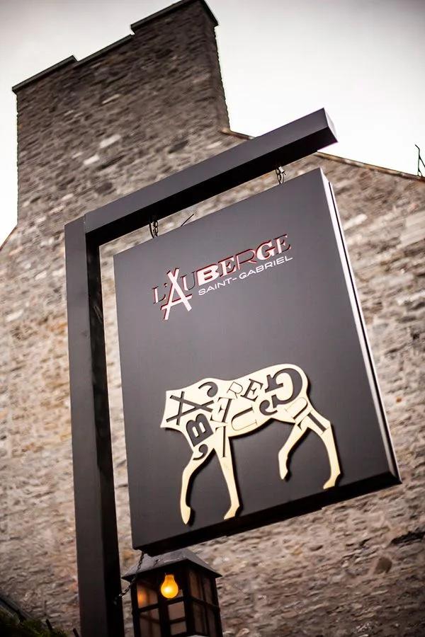 The hanging sign of Auberge Saint-Gabriel above a stone wall in Old Montreal