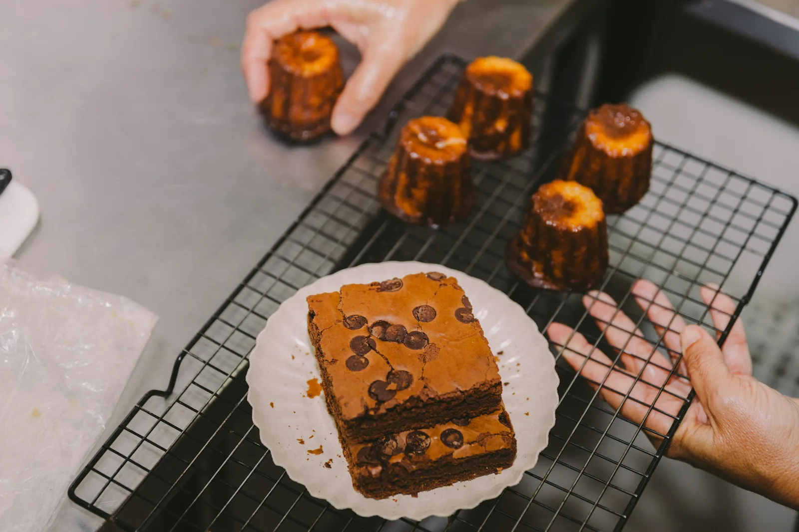Freshly baked canelés cooling on a rack beside a pastry plate