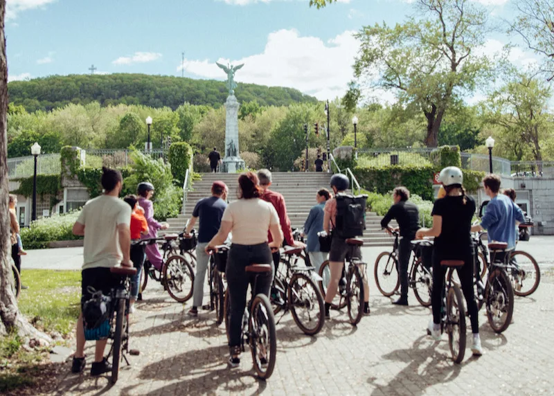 Small group on e-bikes pausing below the Mount Royal monument in Montreal